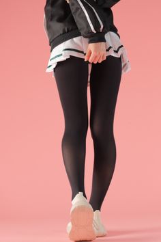 Person in black tights, white skirt, and black jacket against a pink background