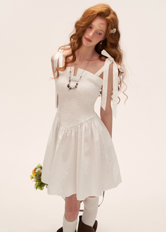 Woman with long red hair and freckles wearing a white dress and holding flowers