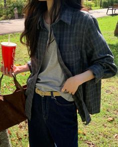 Person in a plaid shirt and jeans holding a Coca-Cola cup in a park