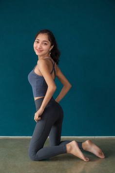 Woman in a yoga outfit kneeling and smiling against a blue wall