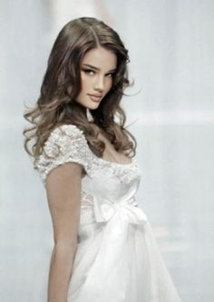 Woman with long curly hair wearing a white wedding dress with a bow