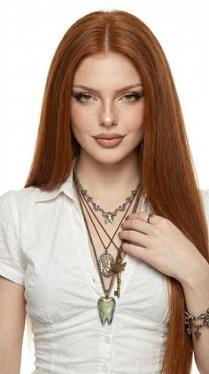 Woman with long red hair and freckles wearing layered necklaces and a white shirt