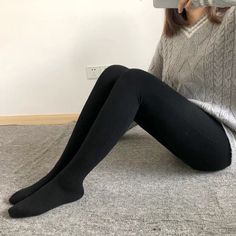 Person wearing black leggings and a gray sweater sitting on a rug