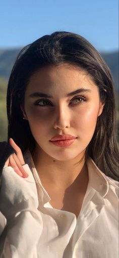 Woman with long dark hair wearing a white shirt outdoors