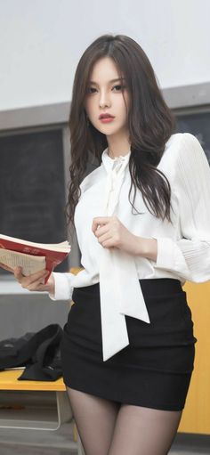 Woman in a white blouse and black skirt holding a book indoors