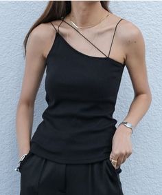 Woman in a black spaghetti strap top and black pants with hands in pockets