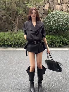 Woman in a black outfit and knee-high boots standing outdoors