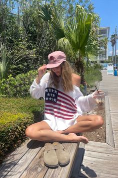 Woman in an American flag sweater and pink hat sitting on a wooden bench outdoors