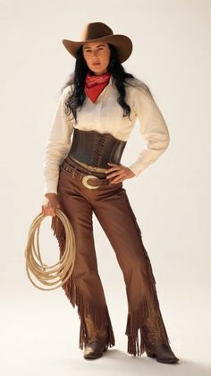 Woman in cowboy attire holding a coiled rope against a plain background