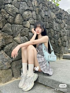 Woman with long black hair and bangs wearing a plaid dress and sneakers, sitting outdoors