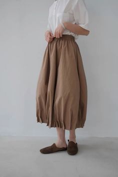 Person in a white shirt and brown skirt with suede slippers indoors
