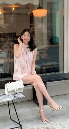 Woman in a pink dress and white heels sitting outdoors with a white handbag