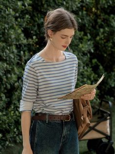 Woman in a striped shirt and jeans holding a map outdoors
