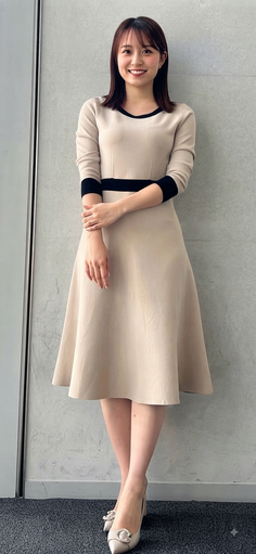Woman in a beige dress with black trim standing indoors and smiling