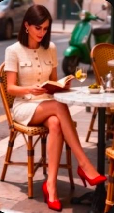 Woman in a tweed dress and red heels reading a book at an outdoor cafe