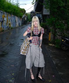 Woman with blonde hair and tattoos wearing a plaid shirt and leather bra on a street