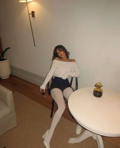 Woman in an off-shoulder sweater and white tights holding a wine glass indoors