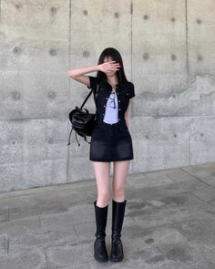 Woman in a black denim jacket and mini skirt with a backpack covering her face