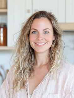 Woman with long wavy blonde hair smiling in a light-colored shirt indoors
