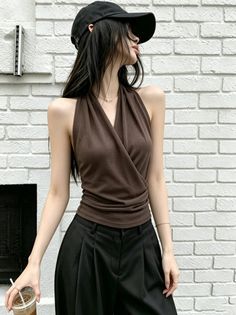 Woman in a brown halter top and black cap against a white brick wall