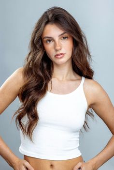 Woman with long brown hair and freckles wearing a white tank top