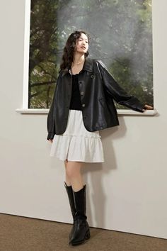 Woman in a black leather jacket and white skirt with long boots indoors