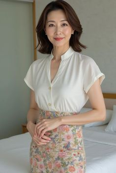 Woman with short hair wearing a white blouse and floral skirt in a bedroom