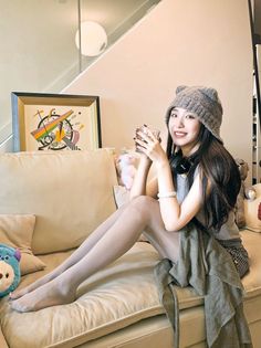 Woman with long hair and a knitted hat sitting on a couch indoors