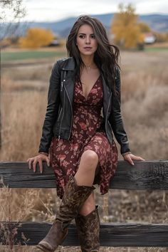 Woman in a leather jacket and floral dress sitting on a wooden fence