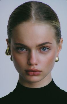 Woman with blue eyes and slicked back hair wearing gold earrings and a black top