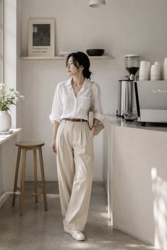 Woman in a white shirt and wide leg pants standing in a minimalist indoor setting