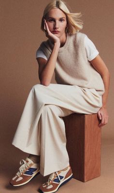 Woman with blonde hair wearing a sweater vest and wide-leg pants, sitting on a wooden block