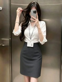Woman in a white shirt and pencil skirt taking a mirror selfie