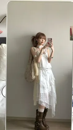 Woman in a white lace dress and brown boots taking a mirror selfie