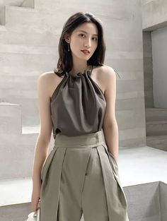 Woman in a dark halter top and pleated pants indoors