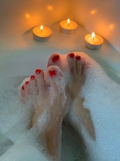 Feet with red nail polish in a bubble bath with lit candles