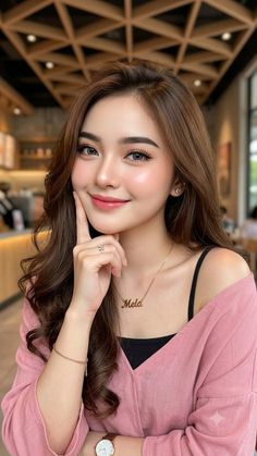 Woman with long brown hair wearing a pink top and a name necklace indoors