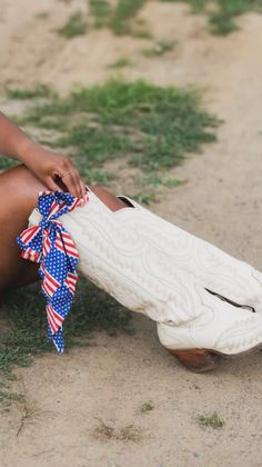 Person wearing white cowboy boots with an American flag bandana tied around their leg