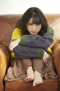 Woman with short hair and bangs wearing a colorful sweater and brown skirt, sitting on a couch