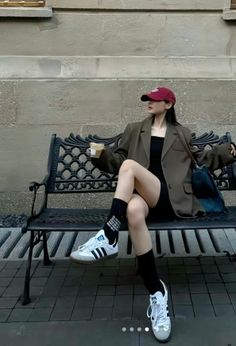 Woman in a red cap and oversized blazer sitting on a bench outdoors