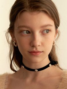 Young woman with long brown hair wearing a black velvet choker and pearl earrings