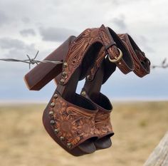 Brown leather high heels with sunflower pattern hanging on barbed wire