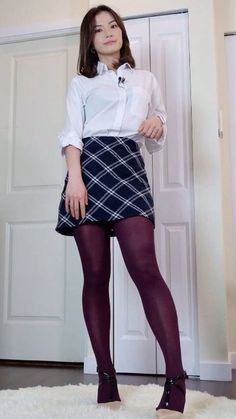 Woman in a white shirt, plaid skirt, and purple tights standing indoors