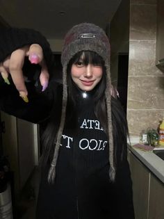 Woman with long black hair and a beanie, showing colorful nails indoors