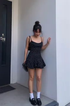 Woman in a black polka dot dress and loafers leaning against a wall
