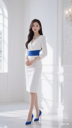 Woman in a white dress with a blue belt and blue heels standing indoors