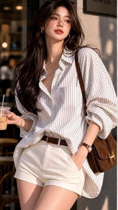 Woman with long hair in a striped shirt and white shorts holding a drink outdoors