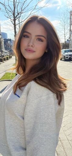 Woman with long brown hair wearing a grey sweatshirt outdoors on a sunny day