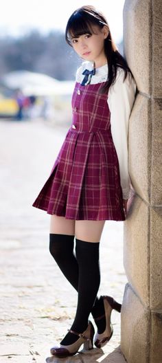 Young woman in a plaid dress and knee-high socks leaning against a wall