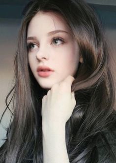 Woman with long dark hair and light eyes, looking away with a soft expression